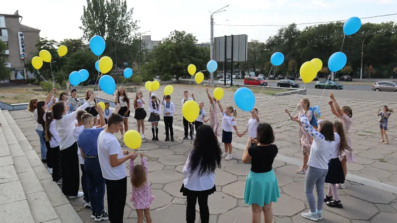 Учні та вчителі стоять колом на площі й тримають синьо-жовті повітряні кулі