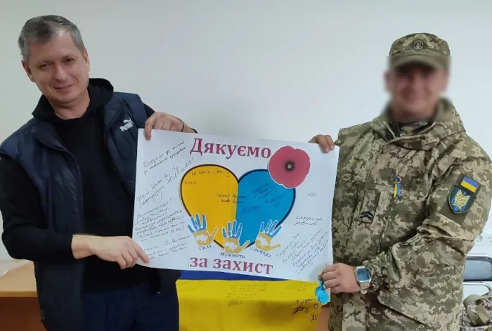 Двоє чоловіків тримають плакат «Дякуємо за захист», зроблений учнями гімназії